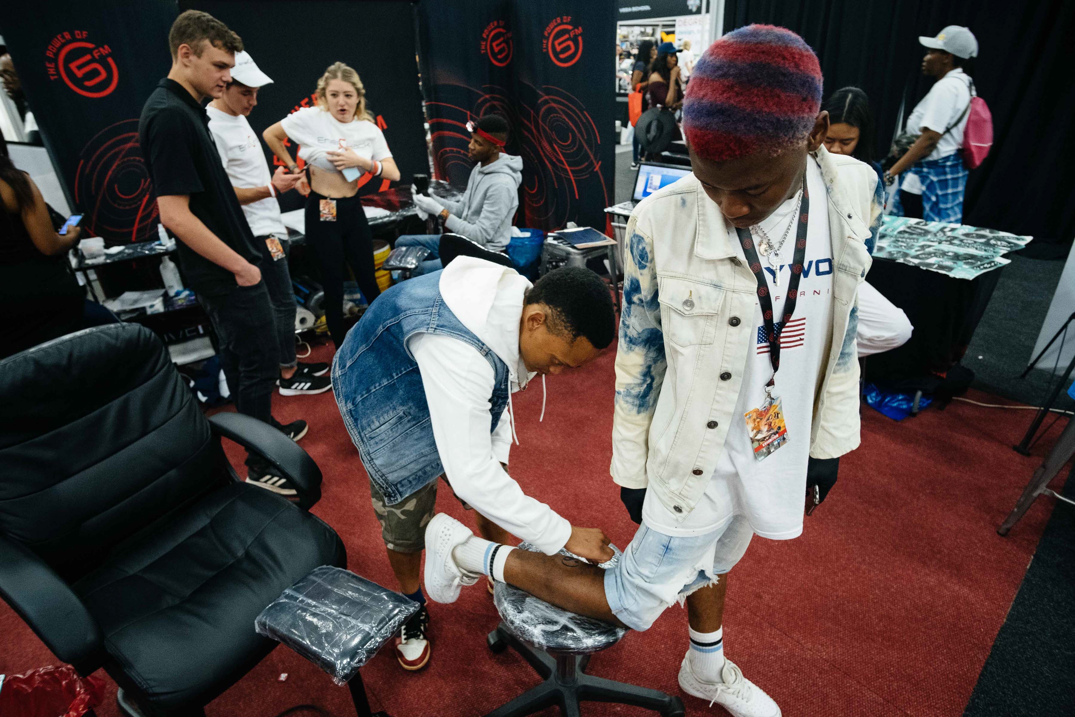 24 September 2019: Brian Thibela from In City Ink Tattoos and Body Piercings sprays a temporary tattoo on Siya Jezile at Comic Con Africa. (Photograph by James Puttick)