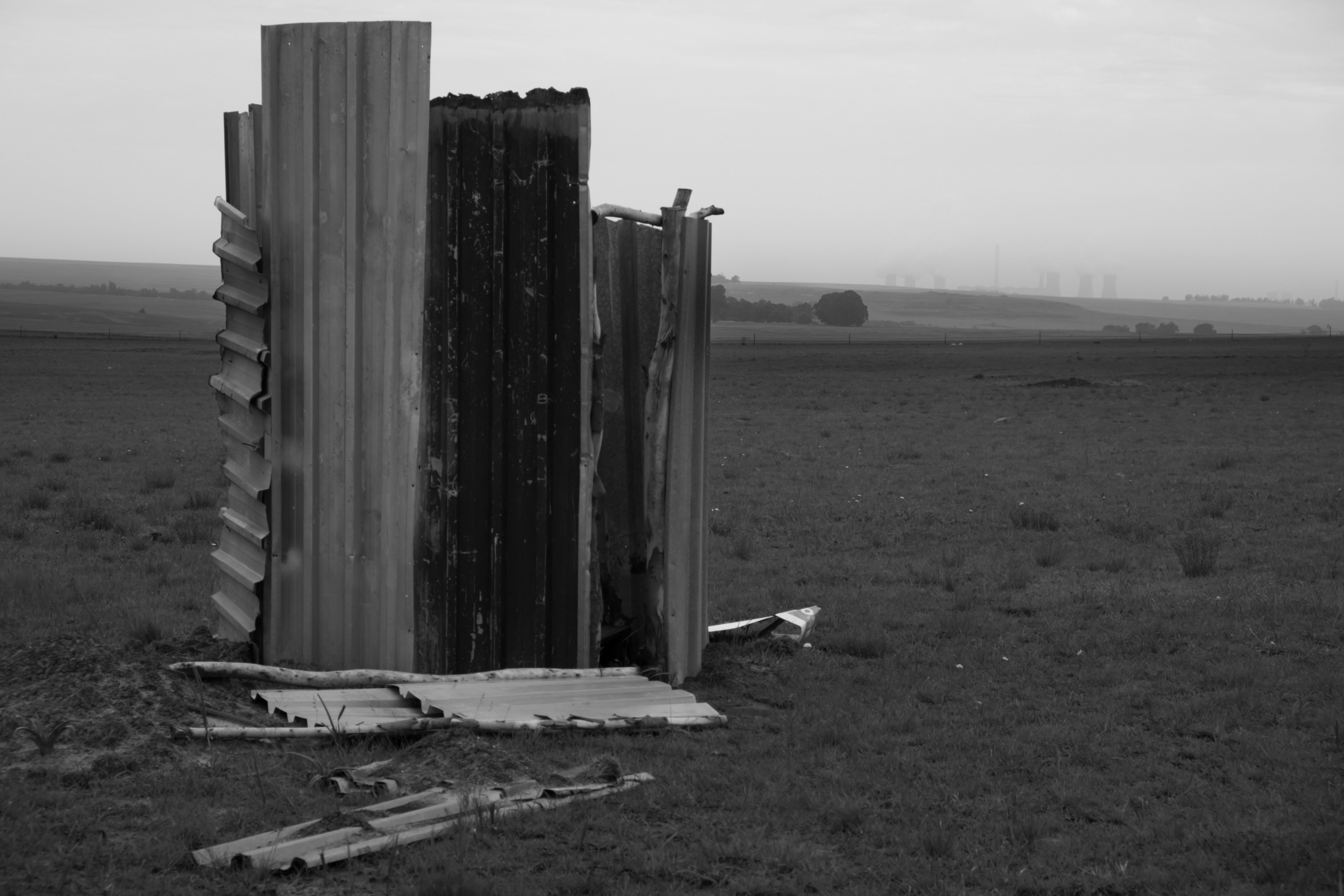 Handmade toilet in field with power station in background. The energy, mining and industrial activity in the province generates billions in revenue, but structural inequality remains entrenched in everyday life. Evander, Mpumalanga.﻿