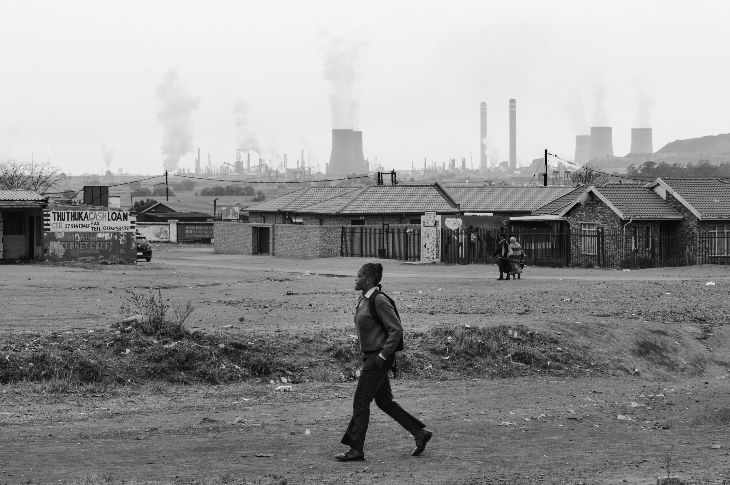 A student walks through eMbalenhle township near Secunda with the Sasol Synfuels Plant in the background. Many people in eMbalenhle suffer from tuberculosis, asthma and other respiratory diseases. eMbalenhle, Mpumalanga.