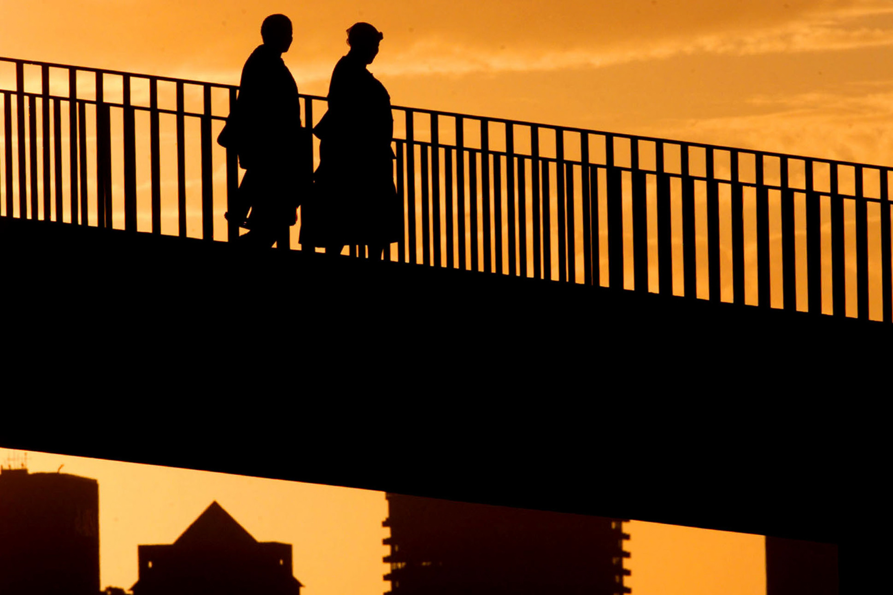 July 2002: Two domestic workers cross a bridge in Cape Town, backlit by the sun setting over the city as they return home. (Photograph by Reuters/ Mike Hutchings)