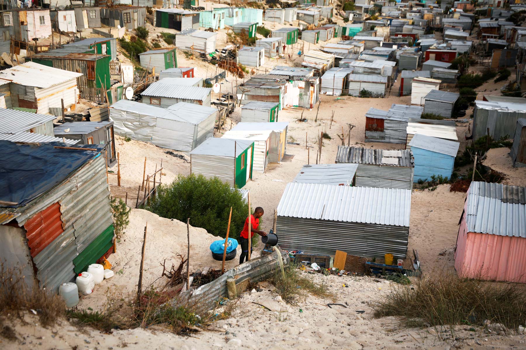 31 March 2020: A child empties a bucket of waste water among shacks in Khayelitsha, Cape Town, during the 21-day stage-five lockdown. (Photograph by Reuters/ Mike Hutchings)