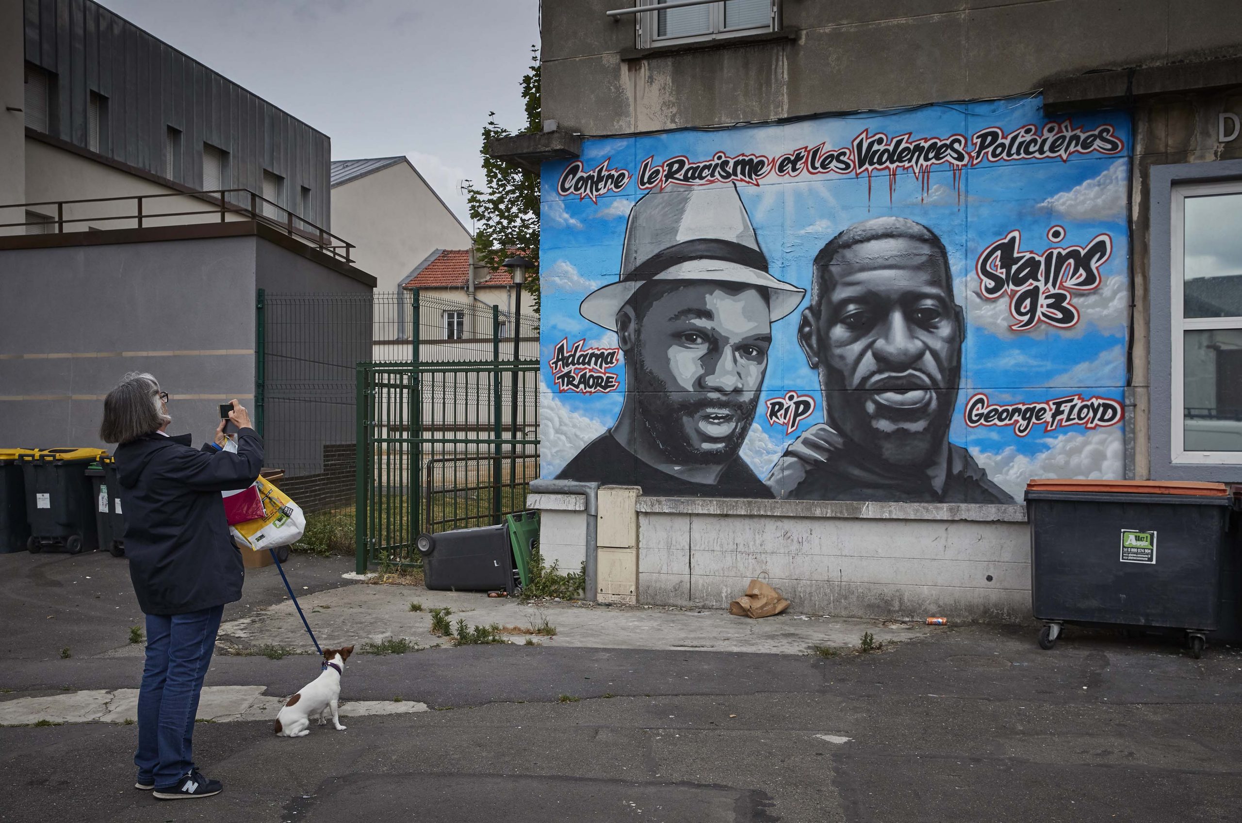 17 June 2020: A woman walking her dog photographs street art paying tribute to murdered American George Floyd (right) and Malian Frenchman Adama Traoré (left) in the Parisian suburb of Stains in Paris, France. (Photograph by Kiran Ridley/ Getty Images)