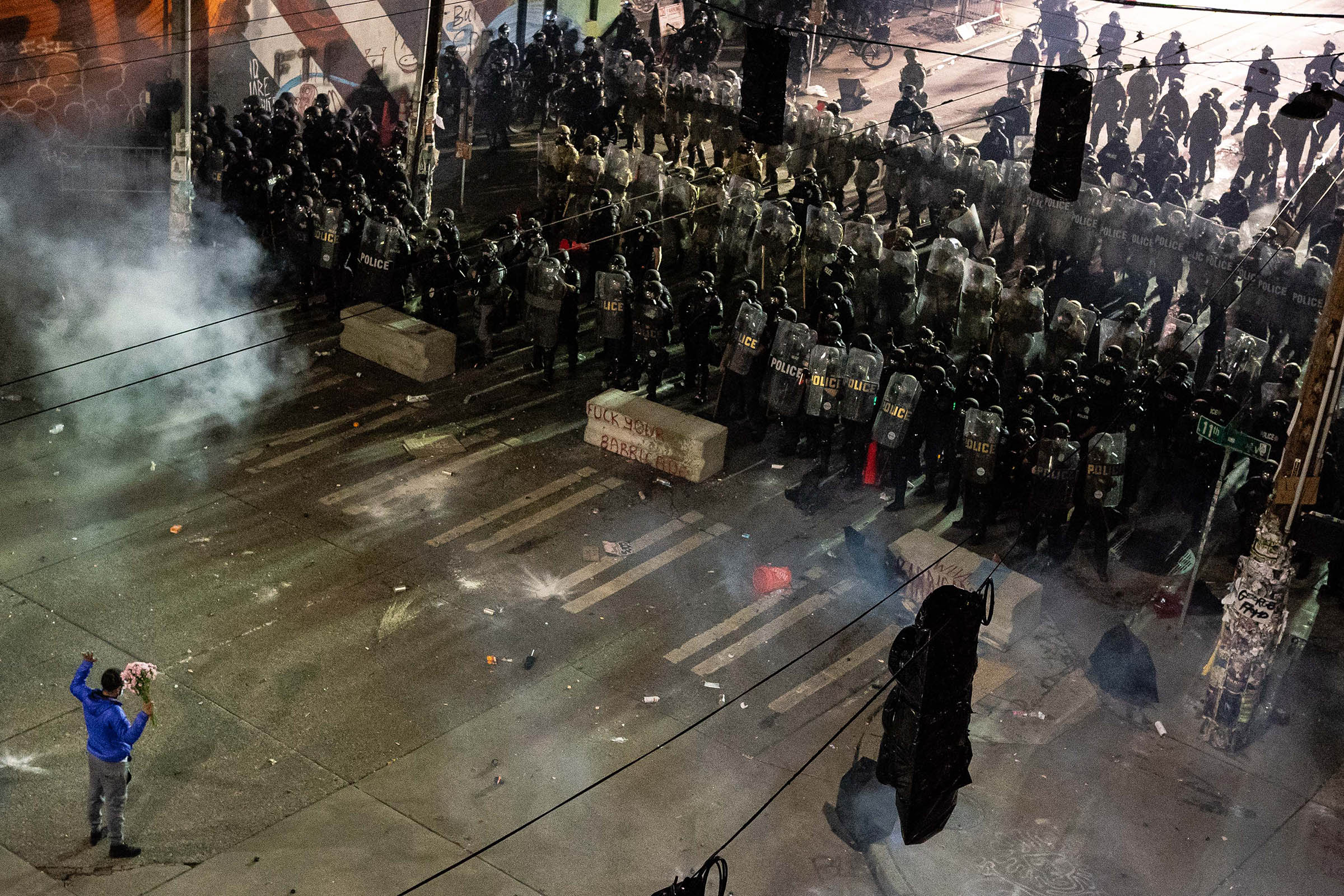 8 June 2020: A Black Lives Matter protester holding a bunch of flowers faces off with police officers near the Seattle Police Department’s East Precinct shortly after midnight in the Washington state city. (Photograph by David Ryder/ Getty Images)