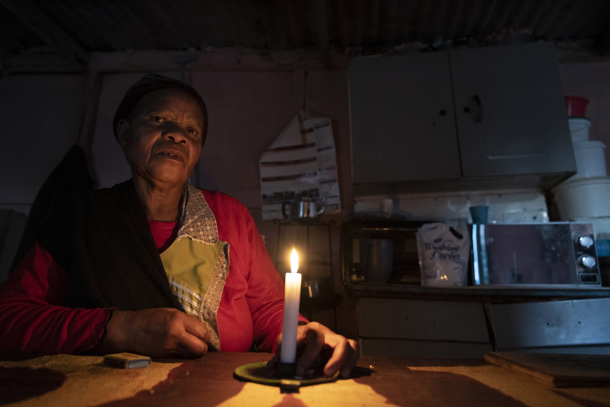 22 June 2020: Thandi Magxotywa inside her shack home in Stjwetla. Electricity supply is erratic and she has to make use of candles for light and a paraffin stove for warmth in winter. (Photograph by Ihsaan Haffejee)