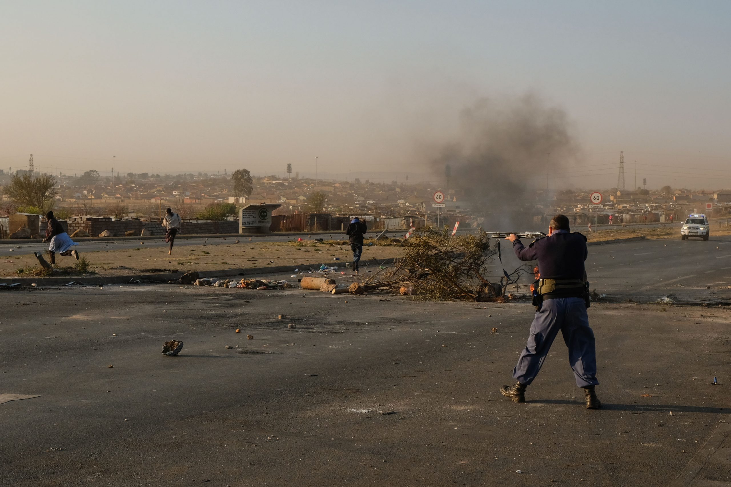 25 August 2020: A South African Police Service officer fires rubber bullets at Doornkop residents who were protesting against the lack of electricity in their shack settlement. 